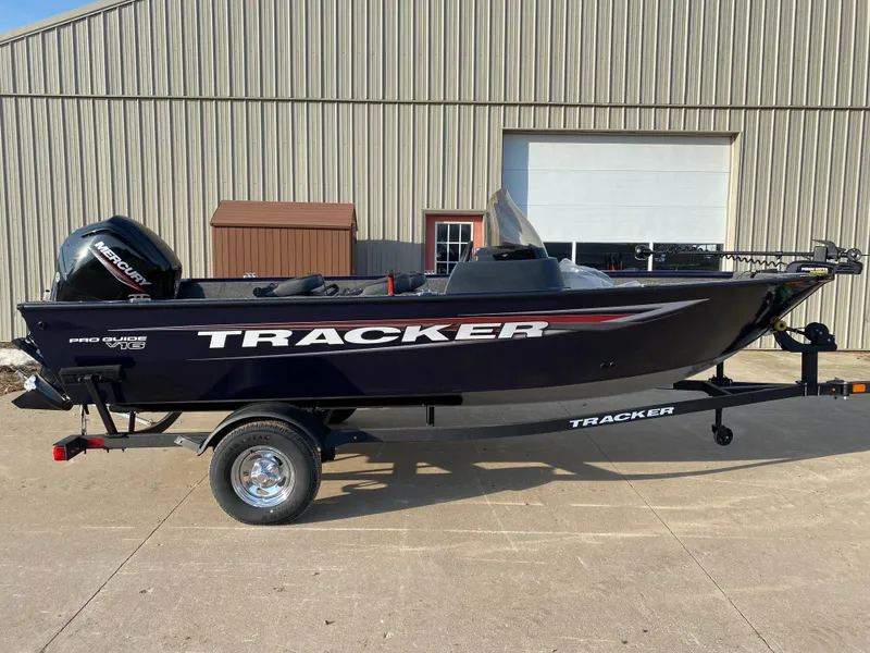 The Image of 2025 Tracker Pro Guide V-16 SC boat on trailer, parked outside a warehouse. - 0