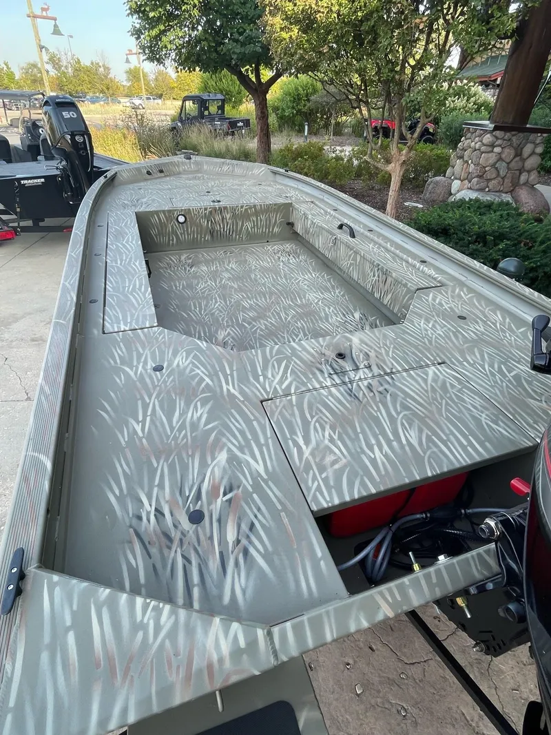 Slide: The Image of 2025 Tracker Grizzly 1654 T Sportsman boat with camouflage design, parked outdoors. - 2