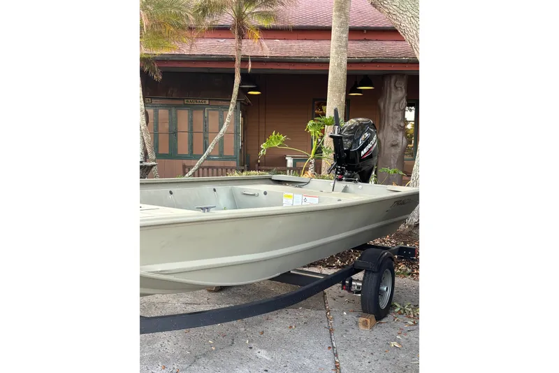 The Image of 2025 Tracker Grizzly 1648 Jon boat on trailer, parked outdoors near trees and building. - 0