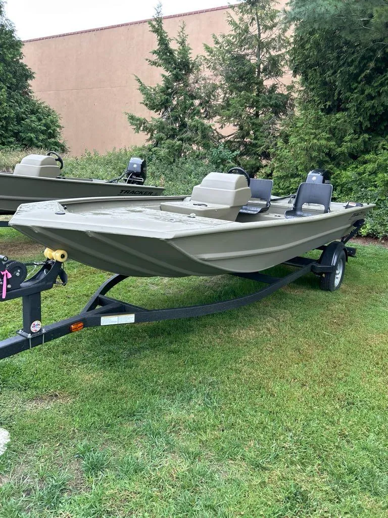 Slide: The Image of 2025 Tracker Grizzly 1754 SC boat on trailer, parked on grass, surrounded by trees. - 2