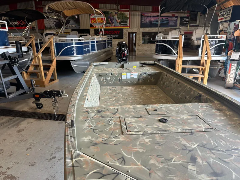 Slide: The Image of 2025 Tracker Grizzly 1648 Jon boat in showroom, camo design, with motor and trailer. - 3