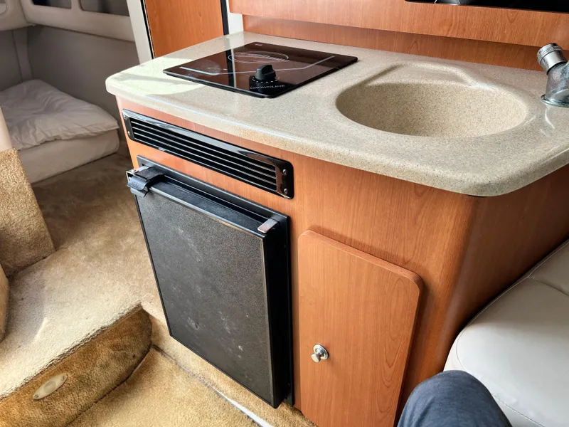 Slide: The Image of 2006 Crownline 250cr boat interior with kitchenette, featuring a sink, stove, and mini fridge. - 10
