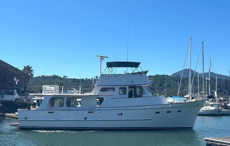 Slide: The Image of 1977 Grand Alaskan Raised Pilothouse yacht docked in a marina under clear blue skies. - 0