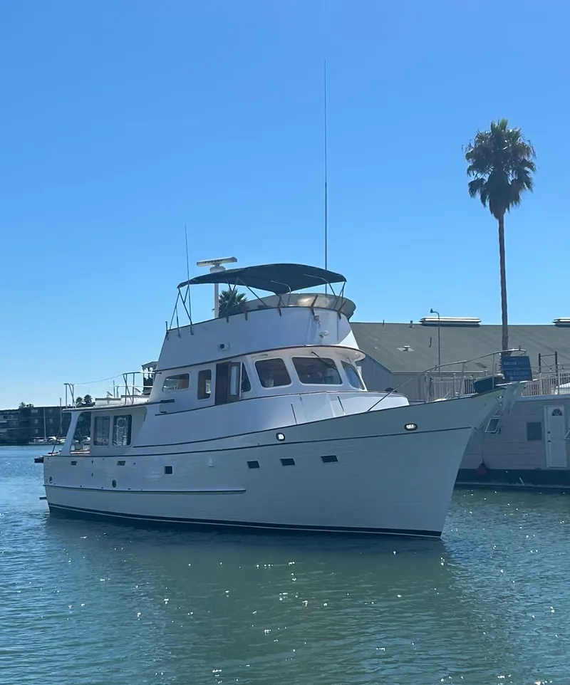 Slide: The Image of 1977 Grand Alaskan Raised Pilothouse yacht on calm water, sunny day, palm tree in background. - 2