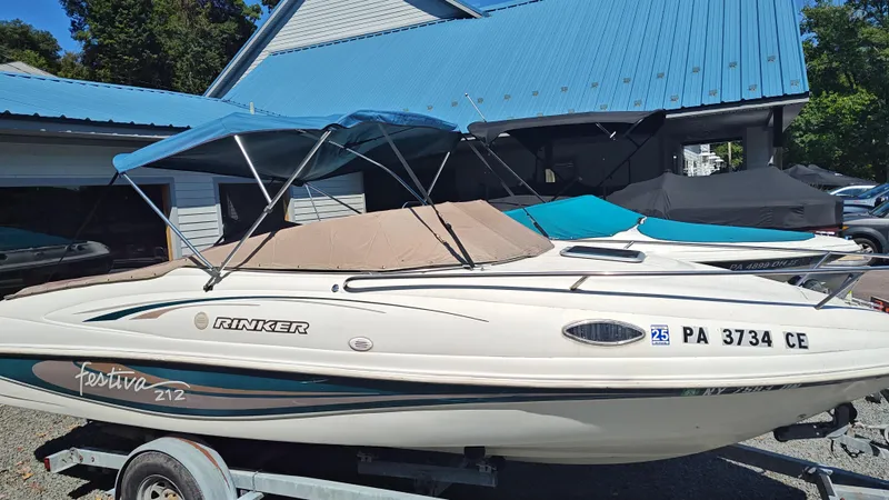 Slide: The Image of 1997 Rinker Festiva 212 boat with blue canopy on trailer, parked near blue-roofed building. - 3