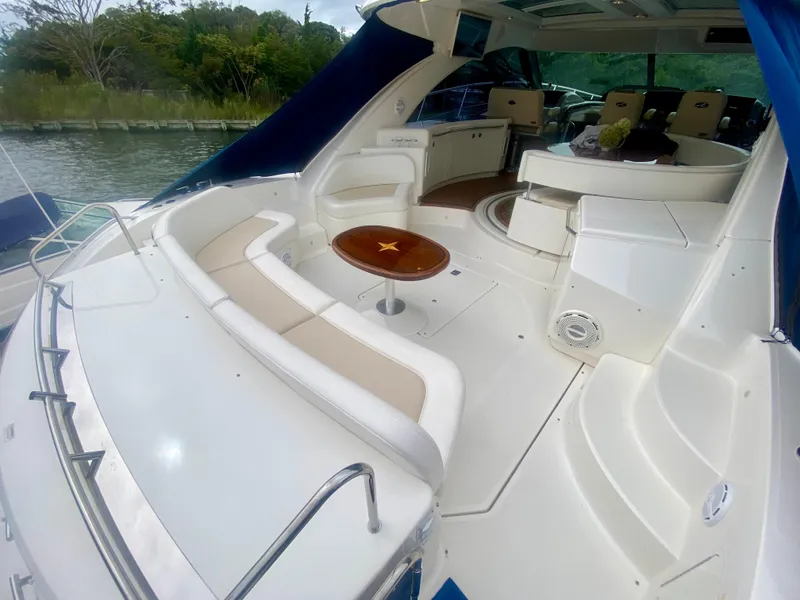 Slide: The Image of 2013 Sea Ray 580 Sundancer yacht interior with seating and table, docked by lush greenery. - 18