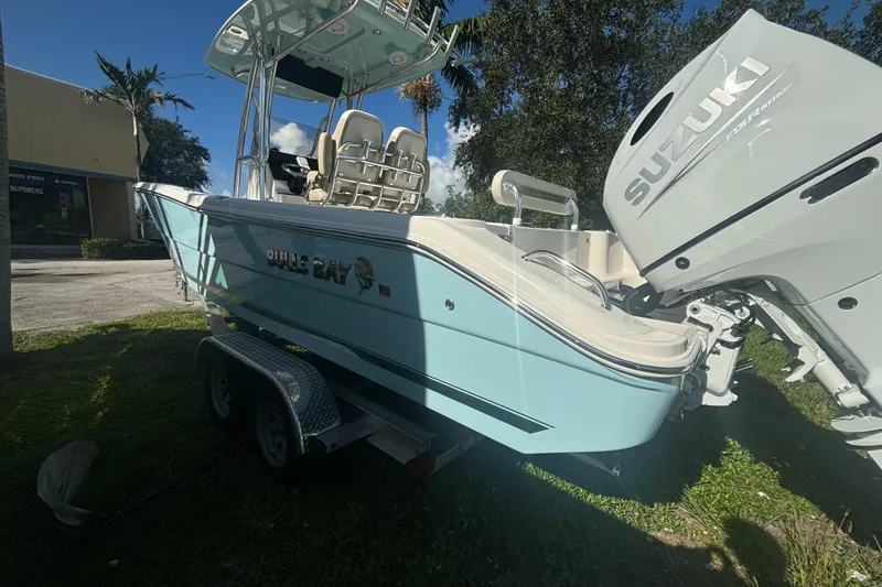 Slide: The Image of 2025 Bulls Bay 255CC boat with Suzuki engine on trailer, parked outdoors. - 2