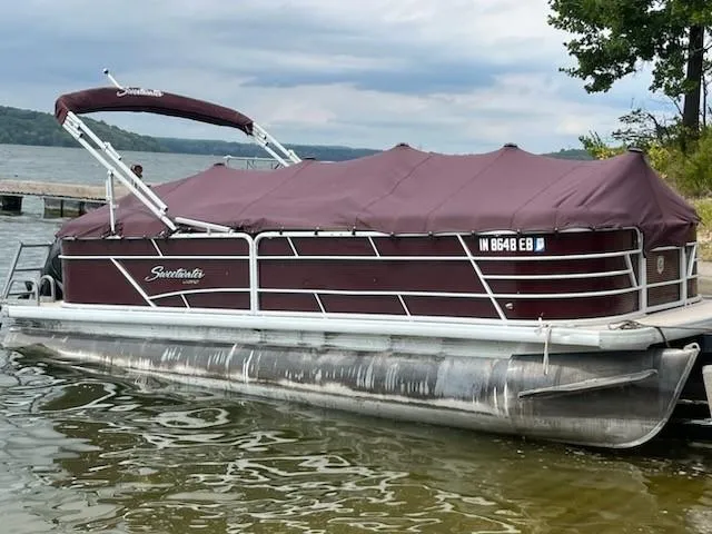 Slide: The Image of 2019 Sweetwater 2286SB pontoon boat with maroon cover docked on a lake. - 0