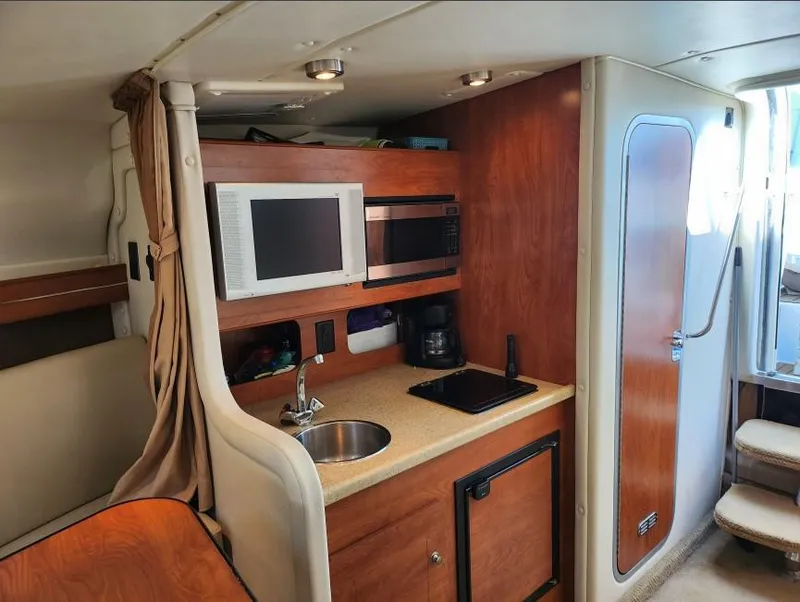 Slide: The Image of 2007 Rinker 300 Express Cruiser interior kitchen with microwave, sink, and wooden cabinetry. - 12