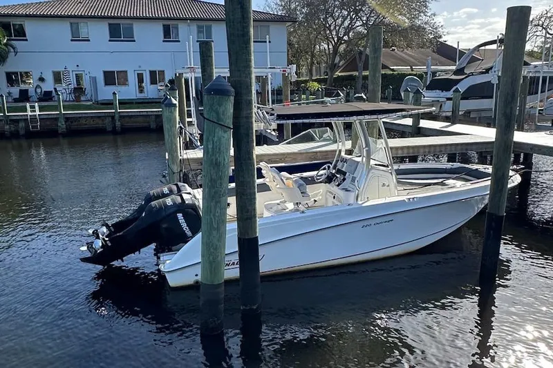Slide: The Image of 2012 Boston Whaler 220 Outrage docked in a marina, featuring dual outboard engines. - 6