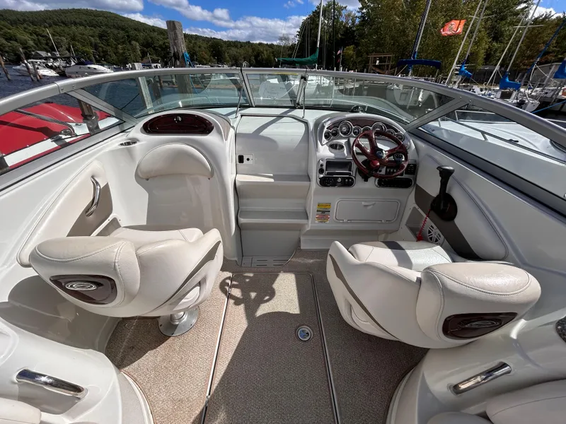 Slide: The Image of 2007 Crownline 255 CCR boat interior with dual seats and dashboard, docked by a scenic lake. - 18