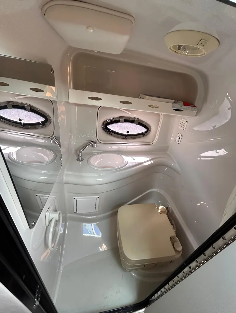 Slide: The Image of 2007 Crownline 255 CCR boat interior bathroom with compact toilet and porthole windows. - 49
