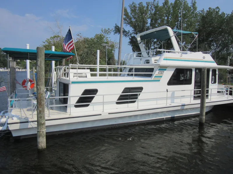 Slide: The Image of 1995 Gibson 44 Classic houseboat docked, featuring American flag and spacious deck. - 3
