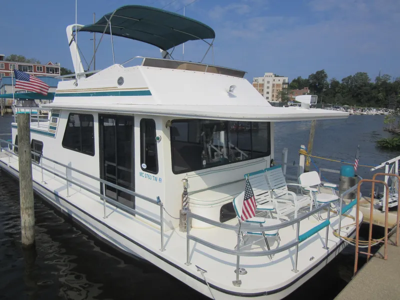 Slide: The Image of 1995 Gibson 44 Classic houseboat docked with American flags, featuring upper deck and seating area. - 4