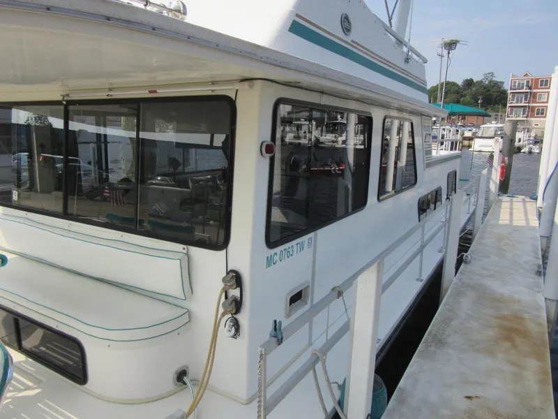 Slide: The Image of 1995 Gibson 44 Classic houseboat docked at marina, featuring spacious windows and white exterior. - 6