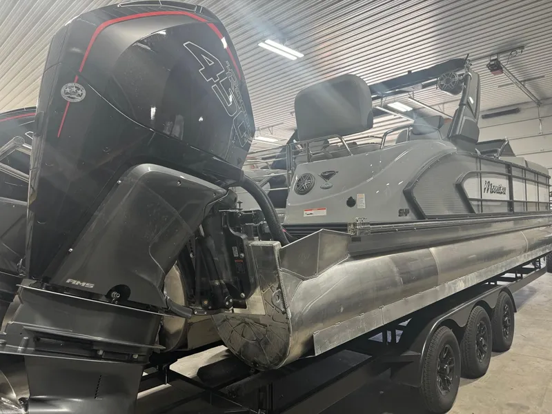 Slide: The Image of 2025 Manitou LX pontoon boat with powerful outboard motor in a garage setting. - 24