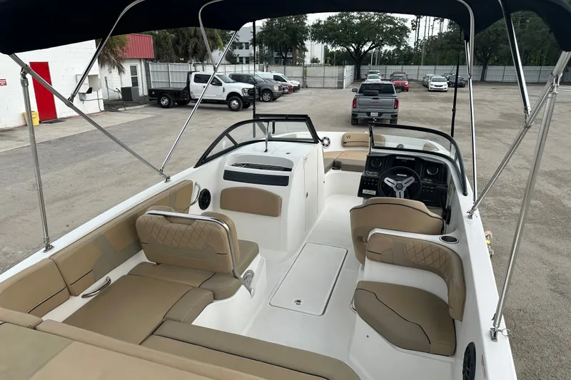 Slide: The Image of 2023 Bayliner VR4 Bowrider OB interior with tan seating and steering wheel, parked outdoors. - 6