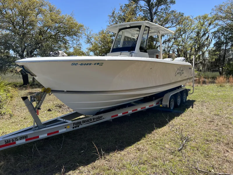 Slide: The Image of 2023 Pursuit S 288 boat on trailer in grassy area, surrounded by trees. - 4