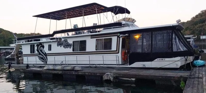 The Image of 1985 Arc Houseboat docked at a marina, featuring a spacious upper deck. - 0