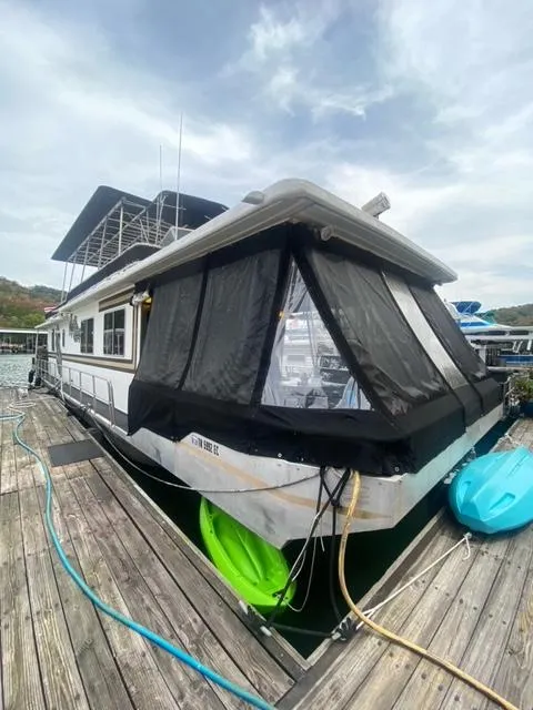 Slide: The Image of 1985 Arc houseboat docked with covered deck and kayaks, under cloudy sky. - 3