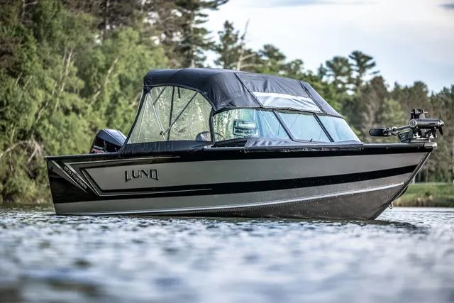 Slide: The Image of 2025 Lund 2075 Fisherman Sport boat on a serene lake with lush greenery. - 1