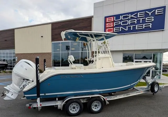 Slide: The Image of 2025 Cobia 220 CC boat on trailer, blue hull, parked outside dealership. - 3