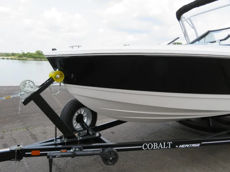 Slide: The Image of 2025 Cobalt CS22 boat on trailer by water, featuring sleek black and white design. - 2