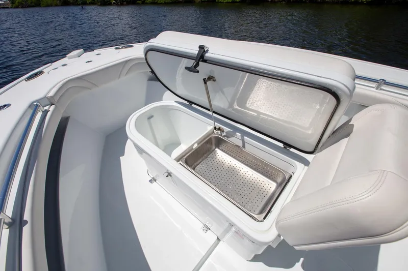 Slide: The Image of 2022 Yellowfin 26 Hybrid boat with open storage compartment, white seating, and water backdrop. - 6