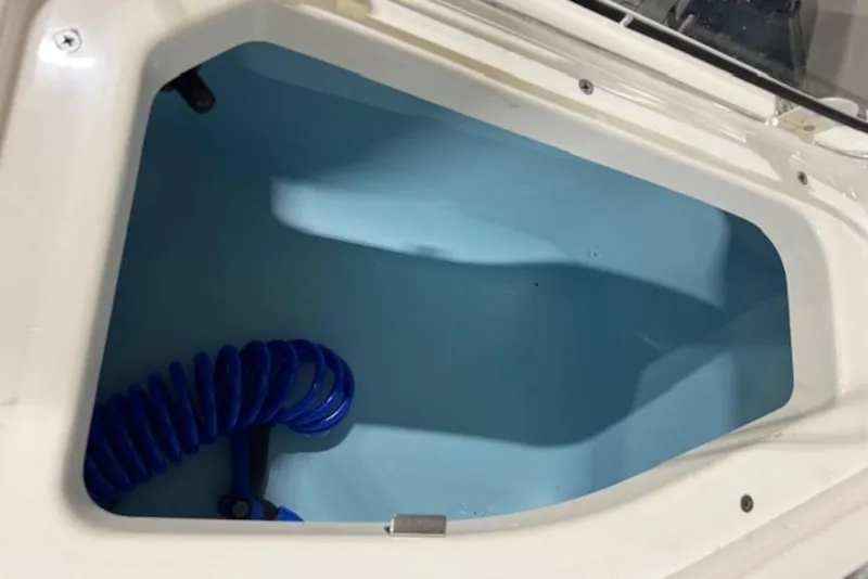 Slide: The Image of Storage compartment of 2025 Yamaha Boats 252 FSH Sport with blue coiled hose. - 14