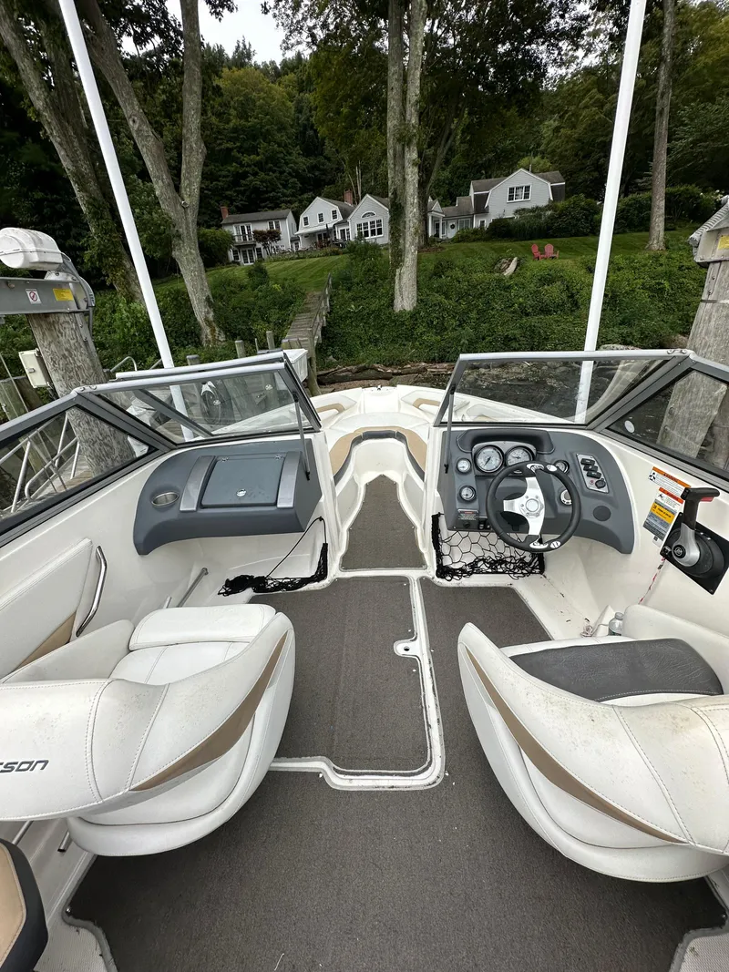 Slide: The Image of 2012 Chaparral 220 SSi boat interior with dual seats and dashboard, docked near lush greenery. - 6