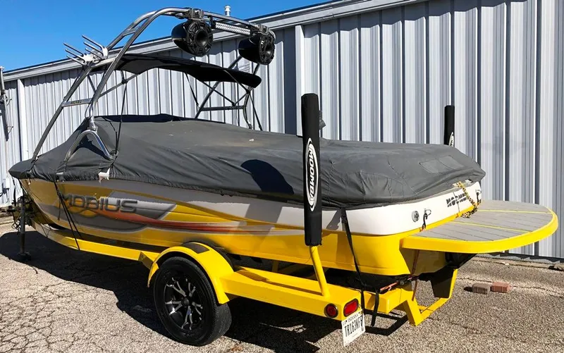 Slide: The Image of 2002 Moomba Mobius LSV boat with cover, yellow and white design, parked on trailer. - 21