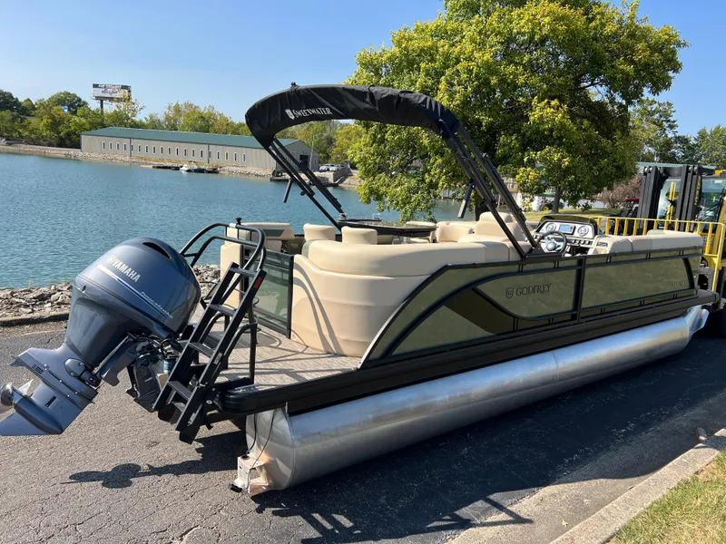 Slide: The Image of 2025 Godfrey SWEETWATER 2286 MT pontoon boat docked by a scenic lake. - 2