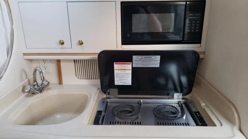 Slide: The Image of Compact kitchen area in a 2000 Sea Ray 290 Sundancer boat with stove, sink, and microwave. - 17