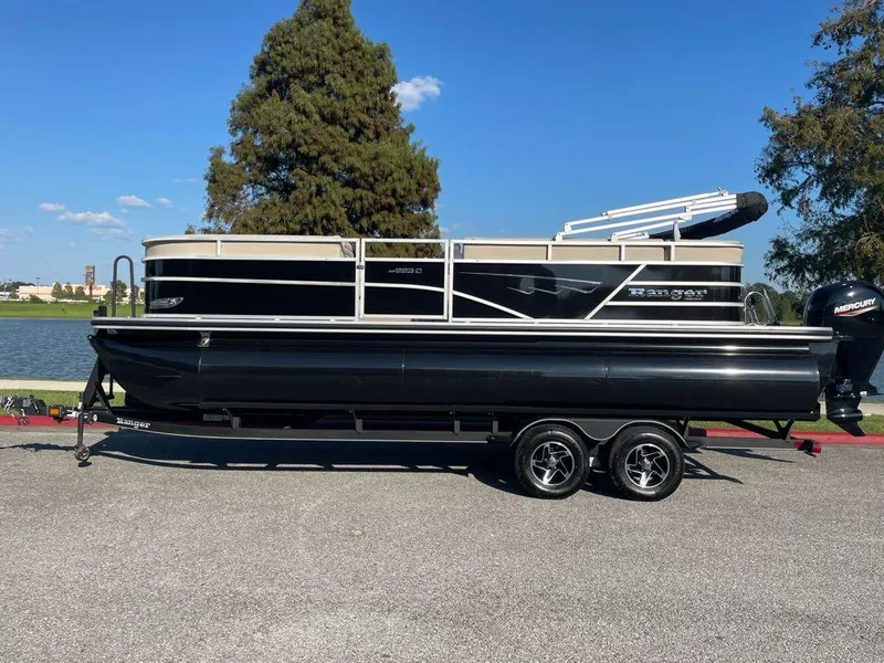The Image of 2024 Ranger Reata 223C pontoon boat on trailer by a lake. - 0