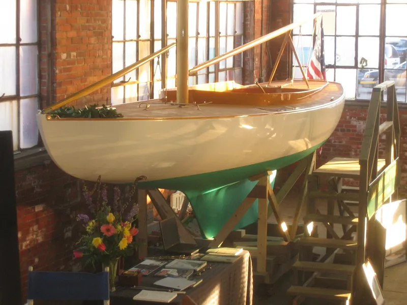 Slide: The Image of 2008 Herreshoff Full-Keel Buzzards Bay 15 sailboat displayed indoors with flowers and brochures. - 14