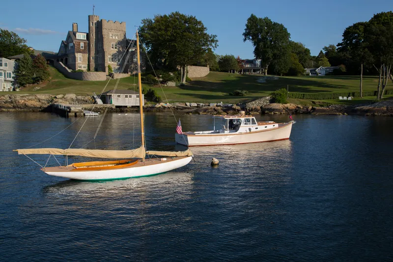 Slide: The Image of Sailboat and motorboat anchored near a historic building, featuring a 2008 Herreshoff Full-Keel Buzzards Bay 15. - 7