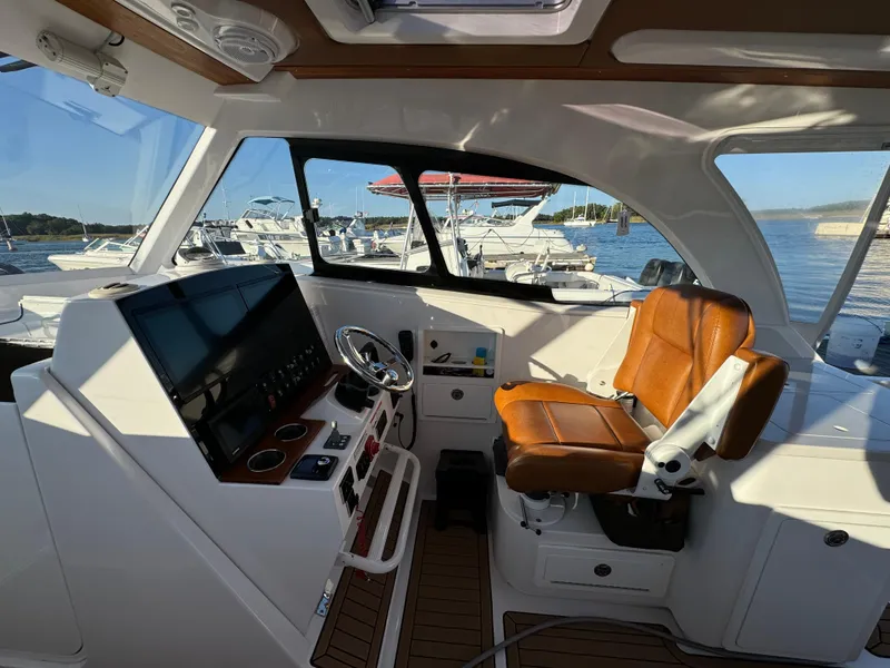 Slide: The Image of 2020 Southport 33 DC boat interior with helm, leather seat, and marina view. - 19