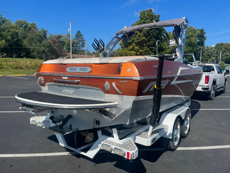 Slide: The Image of Orange MB B52 23 boat on trailer, parked outdoors, sunny day, trees in background. - 3