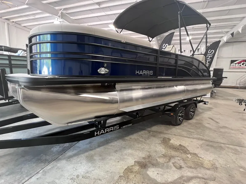 Slide: The Image of 2024 Harris Sunliner 230 pontoon boat in showroom, featuring sleek design and blue exterior. - 2