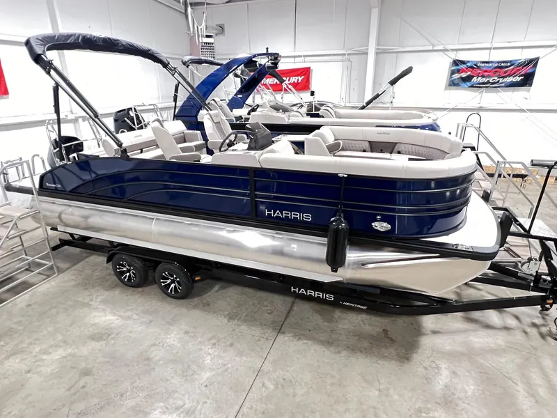 Slide: The Image of 2024 Harris Sunliner 230 pontoon boat in showroom, blue and white exterior, on trailer. - 4