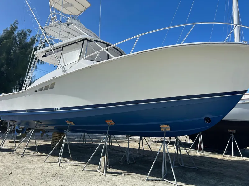 Slide: The Image of 1998 Luhrs 40 Open boat on stands, white and blue hull, clear sky background. - 17