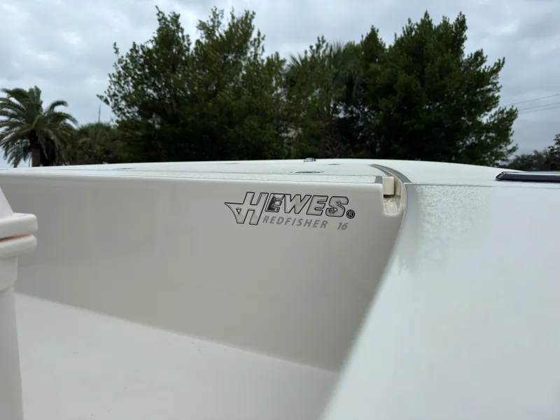 Slide: The Image of 2025 Hewes 16 Redfisher boat detail with logo, outdoors on a cloudy day. - 10