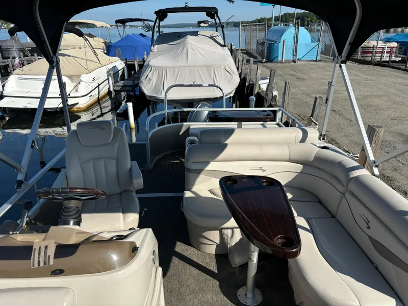 Slide: The Image of 2014 Bennington 24 SSLX pontoon boat with beige seating and wood table, docked at marina. - 6