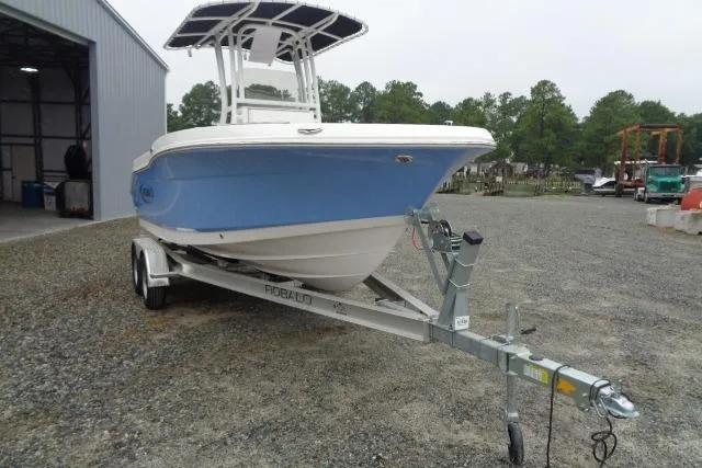 Slide: The Image of 2025 Robalo R200 Center Console boat on trailer, parked outdoors near a warehouse. - 14