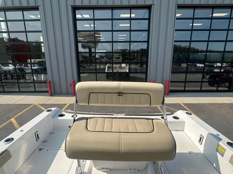 Slide: The Image of 2022 Yamaha Boats 210 FSH® SPORT interior with beige seating, parked outside a showroom. - 7