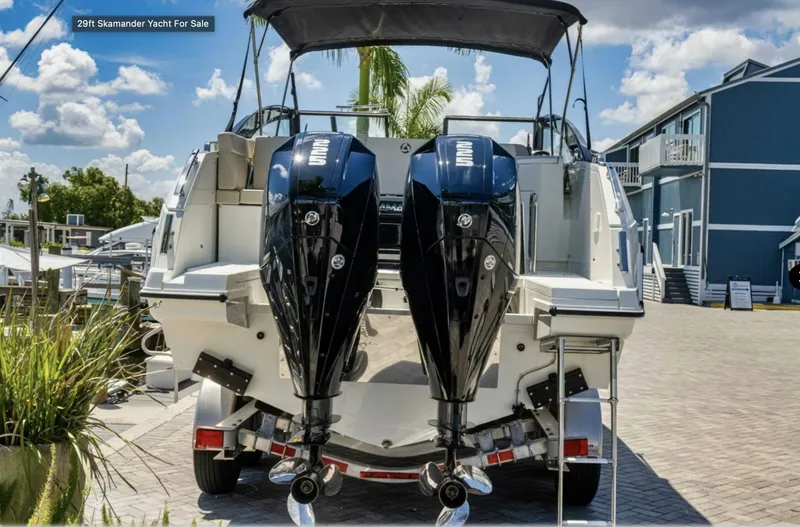 Slide: The Image of 2024 Skamander 850 Voyager boat with dual outboard motors, parked on a sunny day. - 2