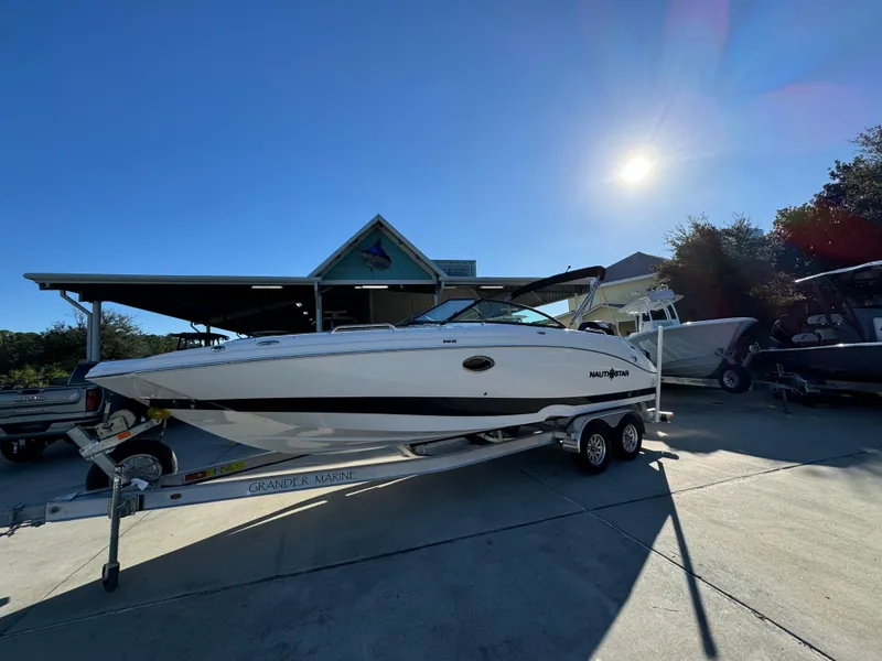 Slide: The Image of 2025 NauticStar 243 DC Deck boat on trailer under sunny sky. - 2