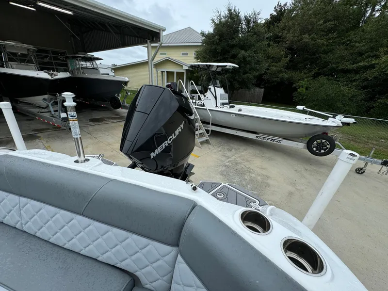 Slide: The Image of 2025 NauticStar 243 DC Deck boat with Mercury engine, parked near other boats. - 24