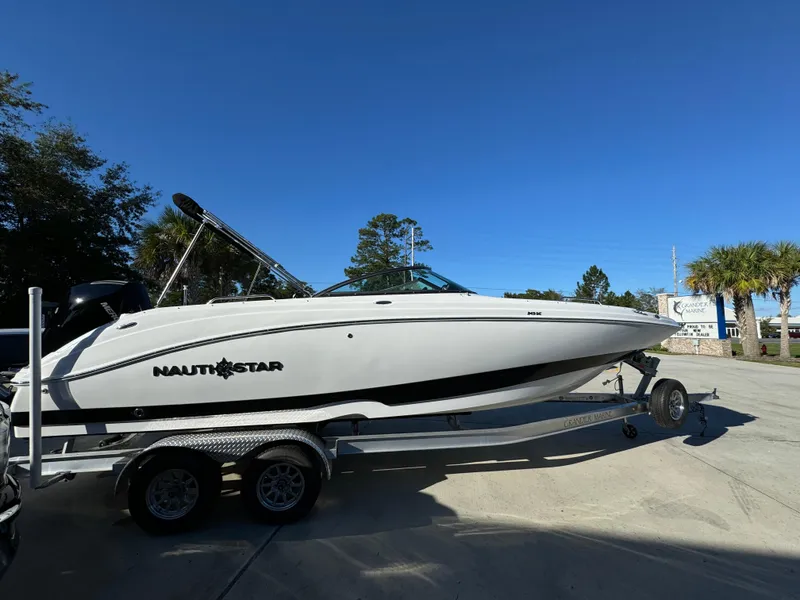 Slide: The Image of 2025 NauticStar 243 DC Deck boat on trailer under clear blue sky. - 6