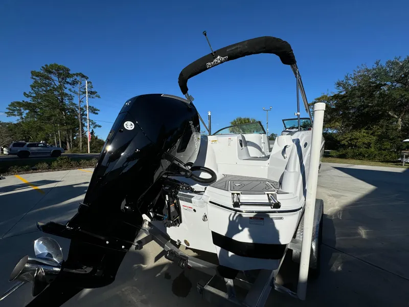 Slide: The Image of 2025 NauticStar 243 DC Deck boat with powerful outboard motor, parked outdoors. - 7